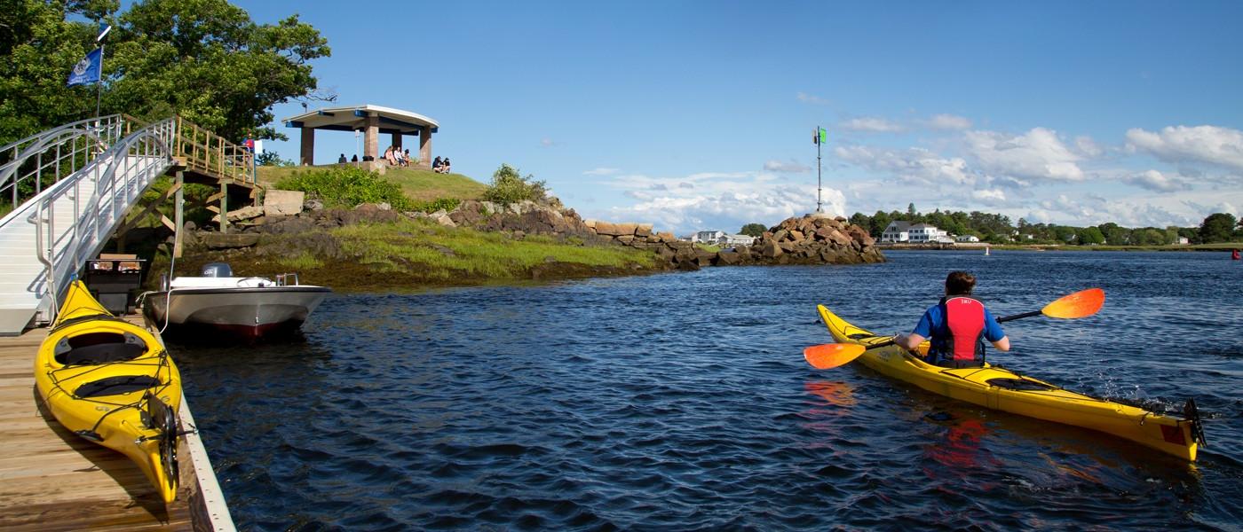 a student paddles a kayak on the ocean along the shoreline of U N E's biddeford campus